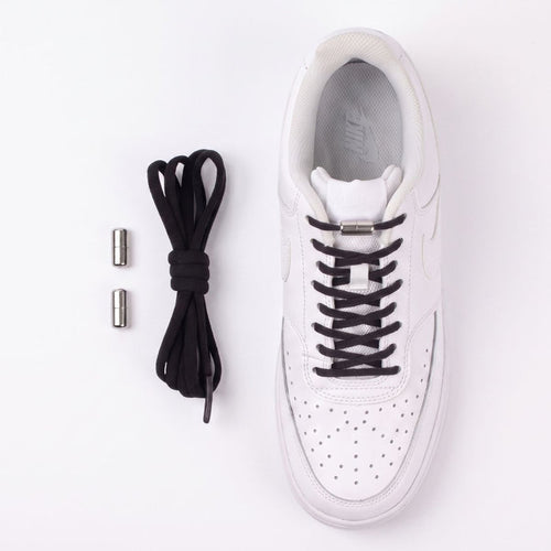 A white Nike sneaker shown from a top-down view on a white background, with black no-tie shoelaces threaded through the eyelets and two small silver metal caps placed to the left.