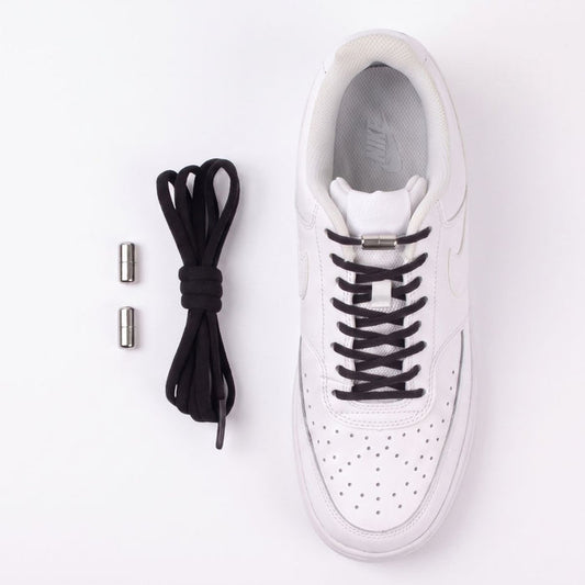A white Nike sneaker shown from a top-down view on a white background, with black no-tie shoelaces threaded through the eyelets and two small silver metal caps placed to the left.