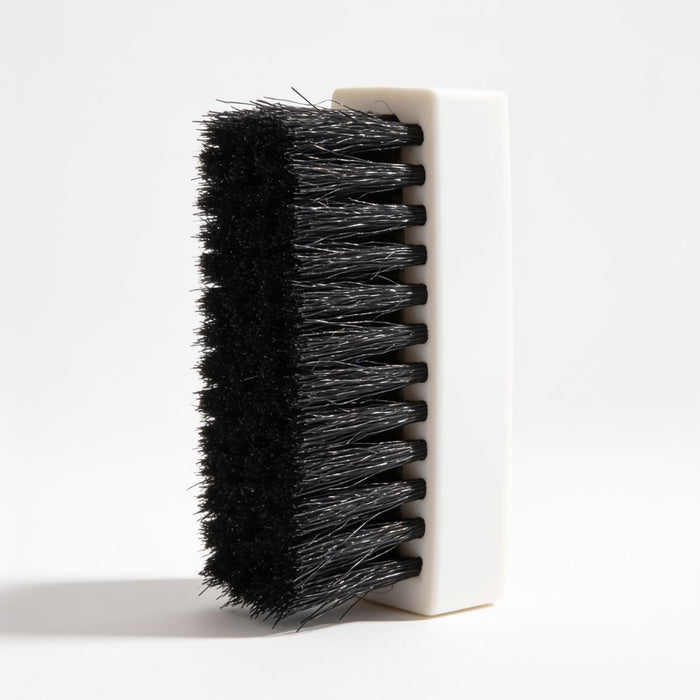 A close-up of a cleaning brush with dense black bristles and a white rectangular handle, shown against a clean white background.